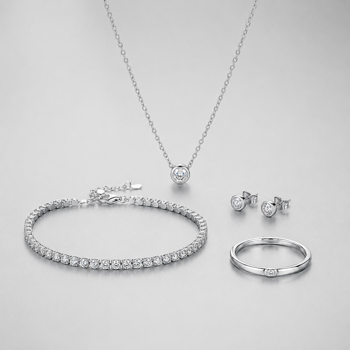 Silver jewelry collection with necklace bracelet earrings and ring on soft gray background